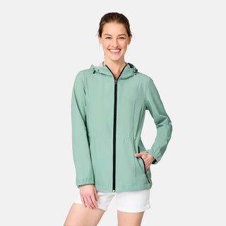 A woman smiles against a plain white background wearing the Free Country Women's X2O Anorak Rain Jacket in light green with a front zipper, paired with white shorts.