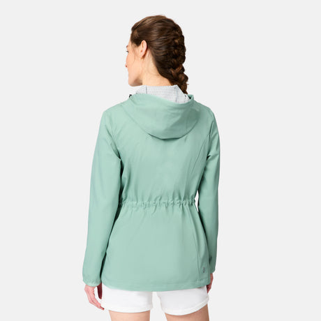 A woman with braided brown hair is seen from behind, wearing the Free Country Women's X2O Anorak Rain Jacket in light green and white shorts, standing against a plain light background.