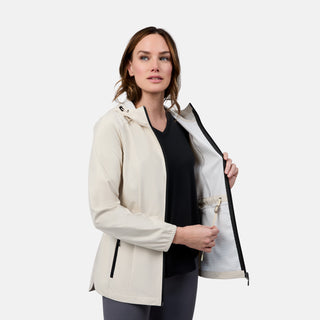 A woman models the Free Country Women's X2O Anorak Rain Jacket in light beige over a black shirt. She stands against a plain background, holding her unzipped jacket open to show the inside pocket.