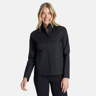 A woman with long blonde hair smiles while wearing the Free Country Women's X2O Packable Rain Jacket in black, paired with matching pants, against a plain light background.
