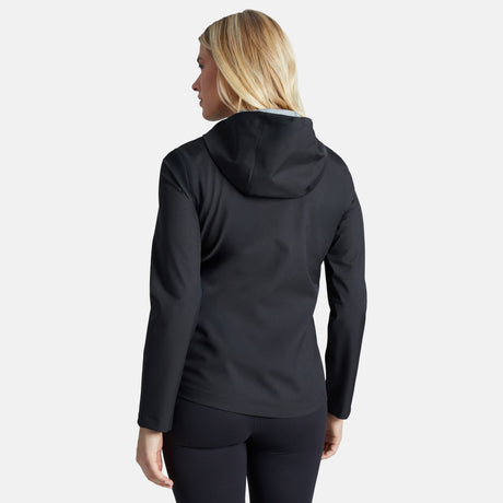 A woman with blonde hair is shown from the back wearing the Free Country Women's X2O Packable Rain Jacket in black and black leggings, standing against a plain light gray background.