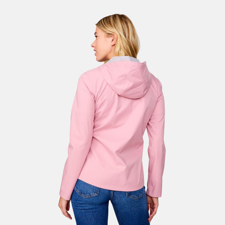 A woman with blonde hair models the Free Country Women's X2O Packable Rain Jacket in pink, paired with blue jeans, looking over her shoulder against a plain white background.