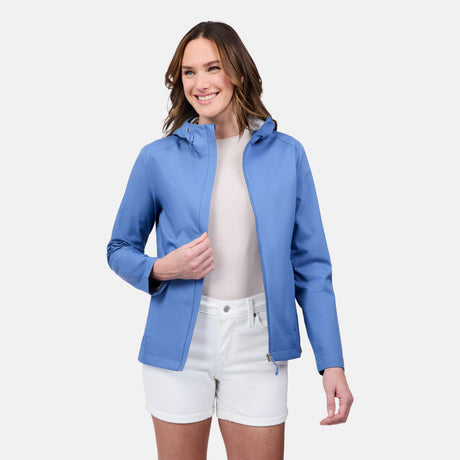A woman smiles against a plain light background, wearing the Women's X2O Packable Rain Jacket by Free Country over a white shirt and white shorts.