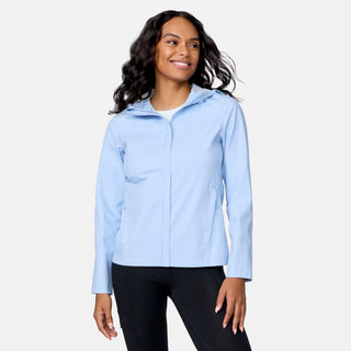 A woman wearing the Free Country Women's X2O Packable Rain Jacket in light blue and black pants stands against a plain background, smiling and looking slightly to the side.
