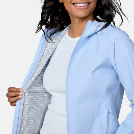 A woman smiles while holding open the Free Country Women's X2O Packable Rain Jacket, revealing its patterned lining over a white shirt.