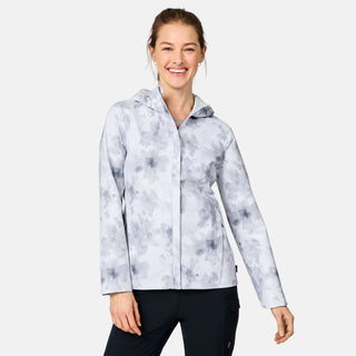 A smiling woman wears the Free Country Women's X2O Packable Rain Jacket, featuring lightweight, breathable fabric and UPF 50+ protection, with black pants, standing against a plain white background.
