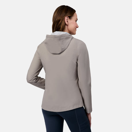 A woman faces away, displaying the back of the Free Country Women's X2O Packable Rain Jacket in light gray with a hood, paired with dark leggings, set against a plain white background.