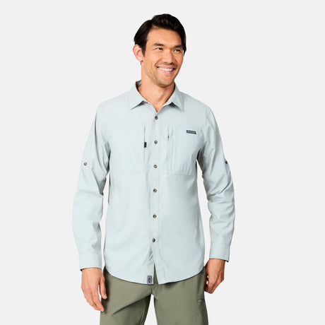 A man with dark hair smiles as he faces forward, wearing the Free Country Men's Acadia Long Sleeve Shirt with two chest pockets and olive green pants—ideal for outdoor adventures—against a plain white background.