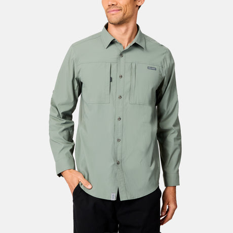 A man wearing a light green Free Country Men's Acadia Long Sleeve Shirt with two chest pockets stands with one hand in his black pants pocket against a plain light background.