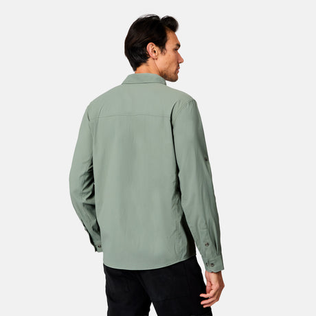 A man stands with his back to the camera, wearing a light green Free Country Men's Acadia Long Sleeve Shirt and black pants against a plain white background.