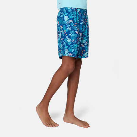 A boy stands barefoot in Free Country Boys' Reel Catch Swim Short, featuring a colorful ocean-themed pattern and quick-drying fabric, shown from mid-torso to feet against a plain white background.