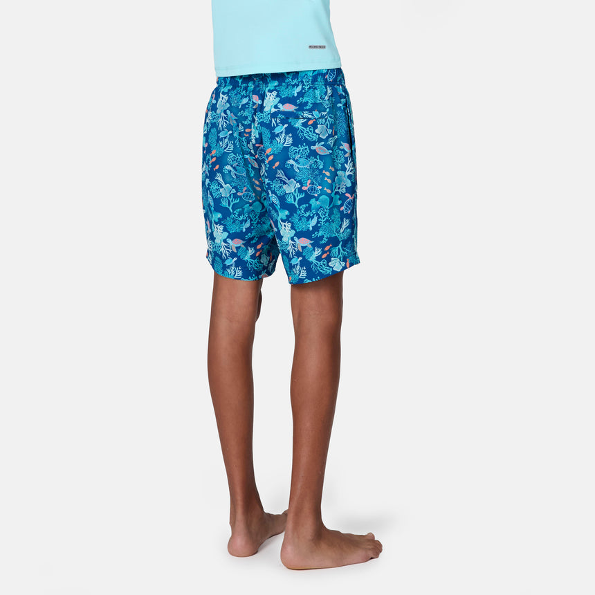 A child stands barefoot, shown from the back in Free Country Boys' Reel Catch Swim Short with quick-drying fabric and a light blue shirt, set against a plain white background.
