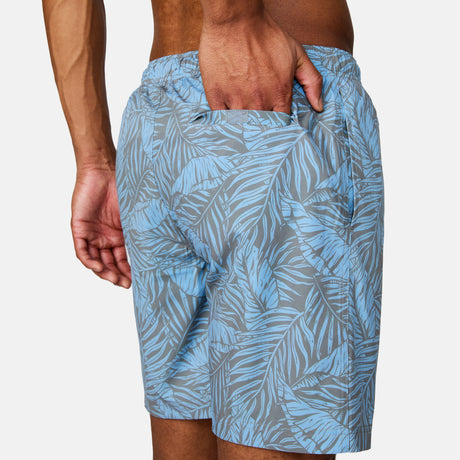 [Josiah is 6'3" wearing a size Medium.] Man wearing Free Country Men's Palm Heaven Swim Short in Bluestone Plam Heaven, size M, made from lightweight stretch recycled polyester performance fabric featuring a full elastic waistband with a drawcord, UPF and quick dry technology, and side seam pockets #color_bluestone-palm-heaven