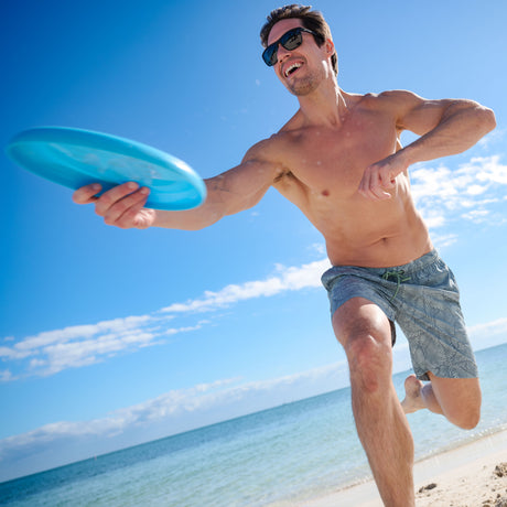 Man playing with a blue frisbee on a beach