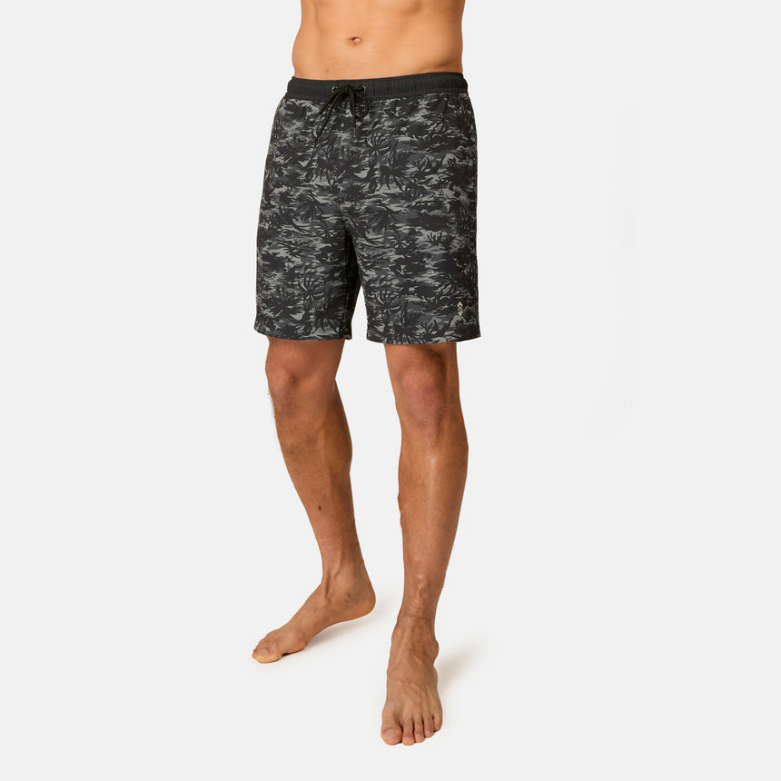 A man stands barefoot in Free Country Men's Surf Camo Swim Short with a drawstring waistband, featuring black and grey camo print and UPF 50+ sun protection, against a plain white background. His upper body is not shown.