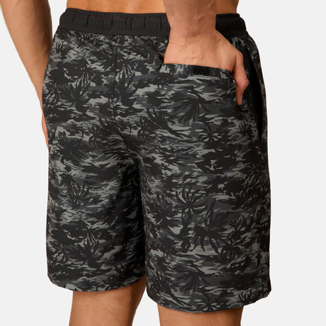 A man models the Free Country Men's Surf Camo Swim Short, shown from the waist down with one hand in the back pocket against a plain background.
