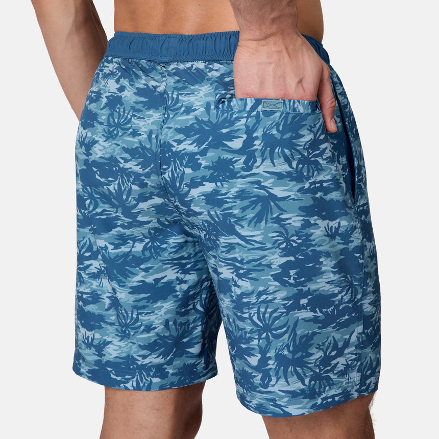 A person wears the Free Country Men's Surf Camo Swim Short with an elastic waistband and side pocket, standing against a plain light background. This swim short offers comfort and UPF 50+ protection.