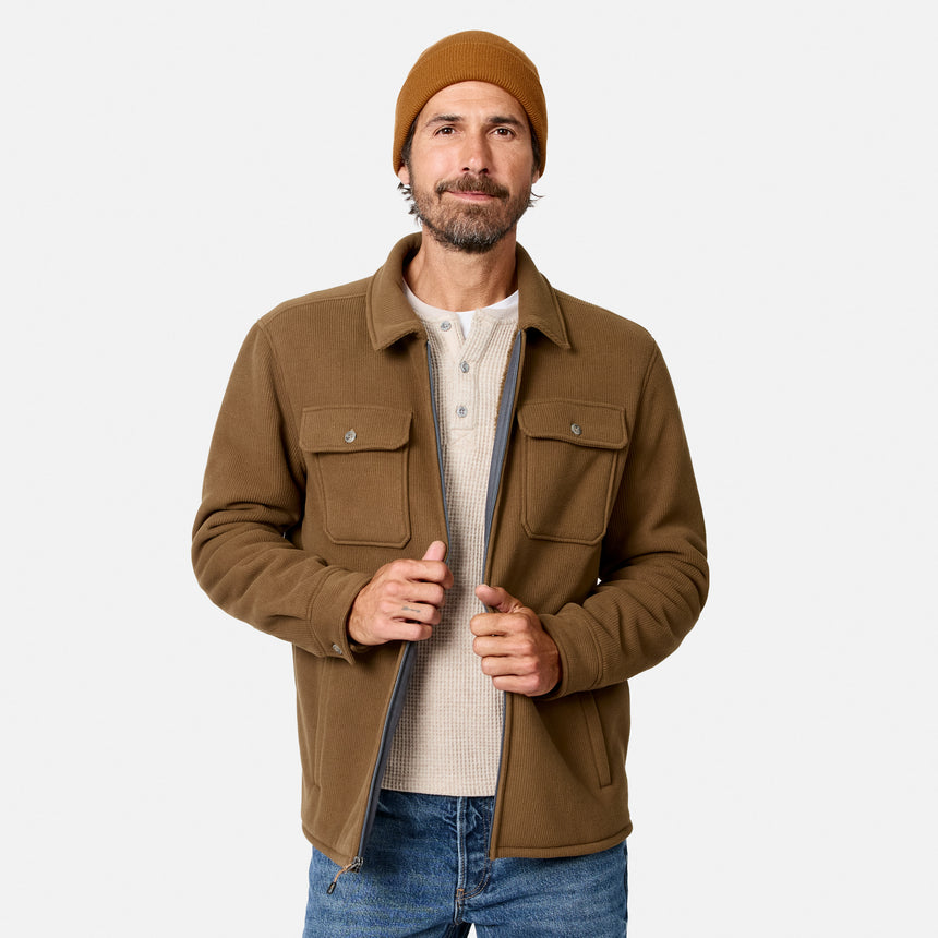 [Model is wearing size M.] A man wearing a brown overshirt jacket over a cream henley shirt, blue jeans, and a brown beanie, standing against a light gray studio background.