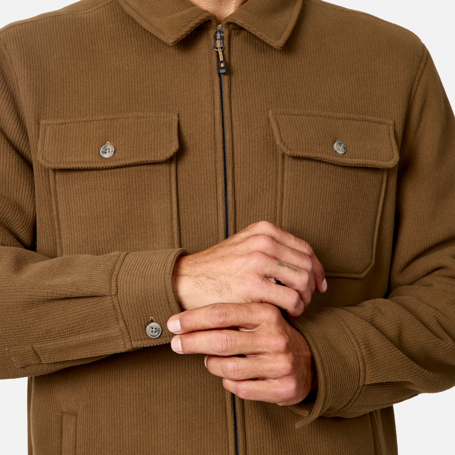 [Model is wearing size M.] A close-up of a person wearing a brown corduroy zip-front jacket with two chest flap pockets and buttoned cuffs, shown against a plain light background.