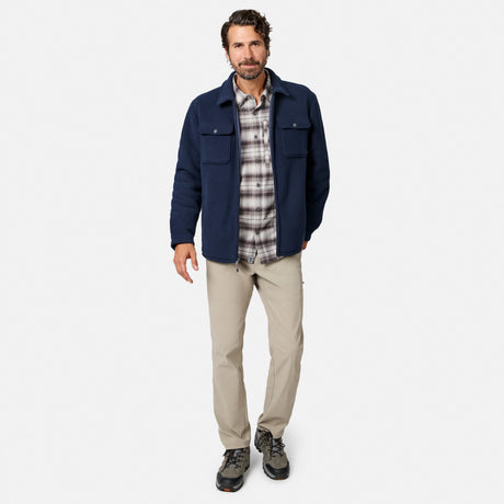 [Model is wearing size M.] A man modeling a navy blue utility jacket over a gray and white plaid flannel shirt, paired with beige hiking pants and dark hiking boots, against a light gray studio background.