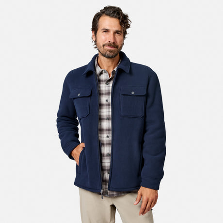 [Model is wearing size M.] A man wearing a navy blue zip-up jacket over a gray and white plaid flannel shirt, paired with beige pants, standing against a light gray studio background.
