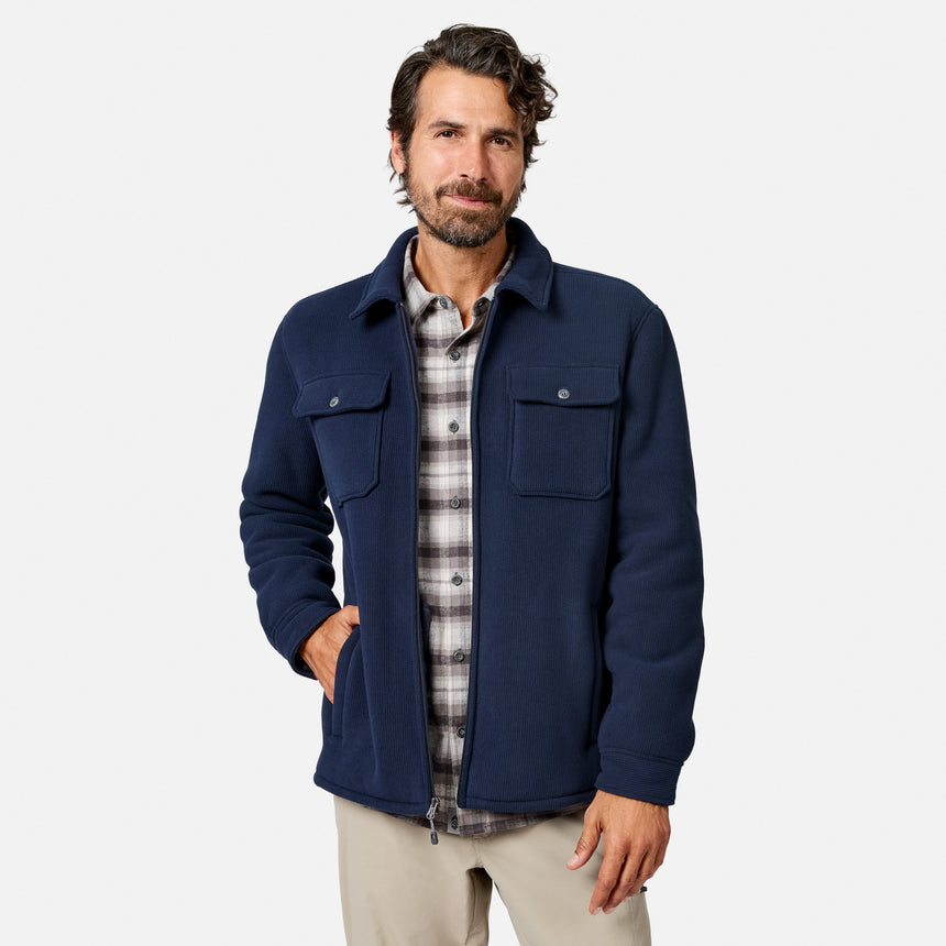 [Model is wearing size M.] A man wearing a navy blue zip-up jacket over a gray and white plaid flannel shirt, paired with beige pants, standing against a light gray studio background.