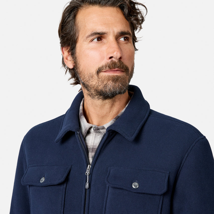 [Model is wearing size M.] A man wearing a navy blue corduroy zip-up jacket over a plaid shirt, photographed against a clean light gray studio background.