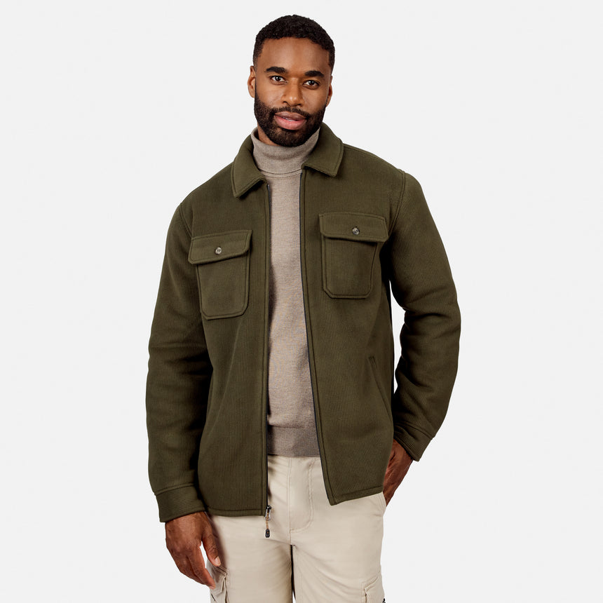 [Model is wearing size M.] A man wearing an olive green jacket over a beige turtleneck sweater and light beige pants, standing against a light gray studio background.