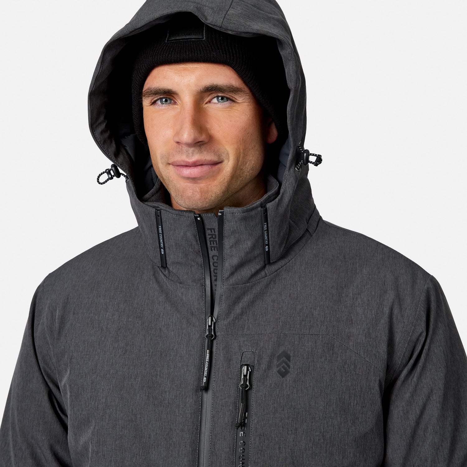 [Model is wearing size M.] A man wearing a dark gray hooded technical jacket and a black knit beanie, shown from the chest up against a light gray studio background.