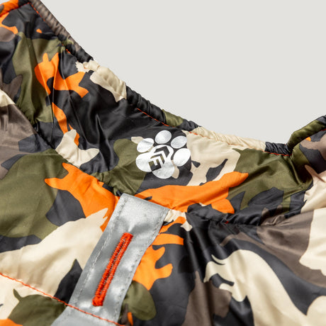 Close-up of the Clearance Dog Down Reversible Mock Jacket, featuring a water-resistant camouflage pattern in green, orange, brown, and black, with a reflective strip and a white paw print logo accented by geometric shapes.