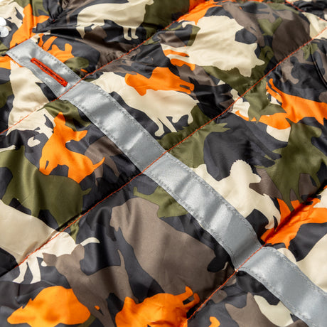 Close-up of the Clearance Dog Down Reversible Mock Jacket, a water-resistant, quilted jacket with green, orange, beige, and black camouflage featuring animal silhouettes and a shiny silver reflective strip across the fabric.