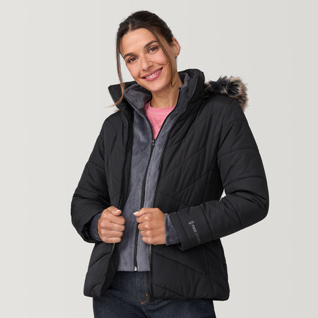 [Olga is 5’9" wearing a size Small.] Woman wearing Free Country Women's Brisk II Parka Jacket in black with a full front zipper opening, soft lining, attached hood with faux fur trim, recycled polyester fill, and water resistant and wind resistant stretch performance fabric, light grey background. Perfect women’s  jacket for fall weather.