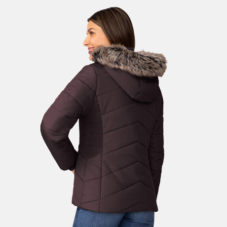 A woman faces away, wearing the Free Country Women's Brisk II Parka Jacket—crafted from recycled plastic—with blue jeans, against a plain light background.