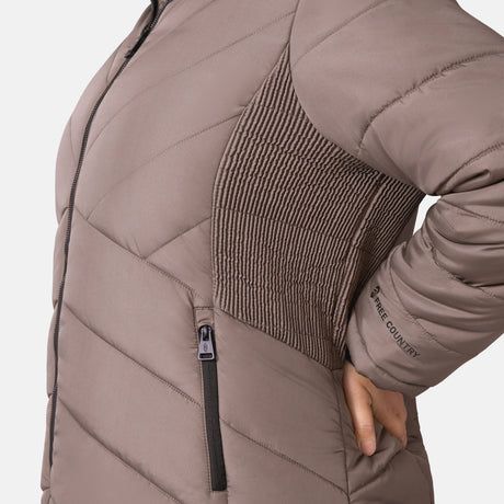 [Lola is 5'10.5" wearing a size 1X.] Woman wearing Free Country Women's Brisk II Parka Jacket in brown with a full front zipper opening, soft lining, attached hood with faux fur trim, recycled polyester fill, and water resistant and wind resistant stretch performance fabric, light grey background. Perfect women’s  jacket for fall weather.