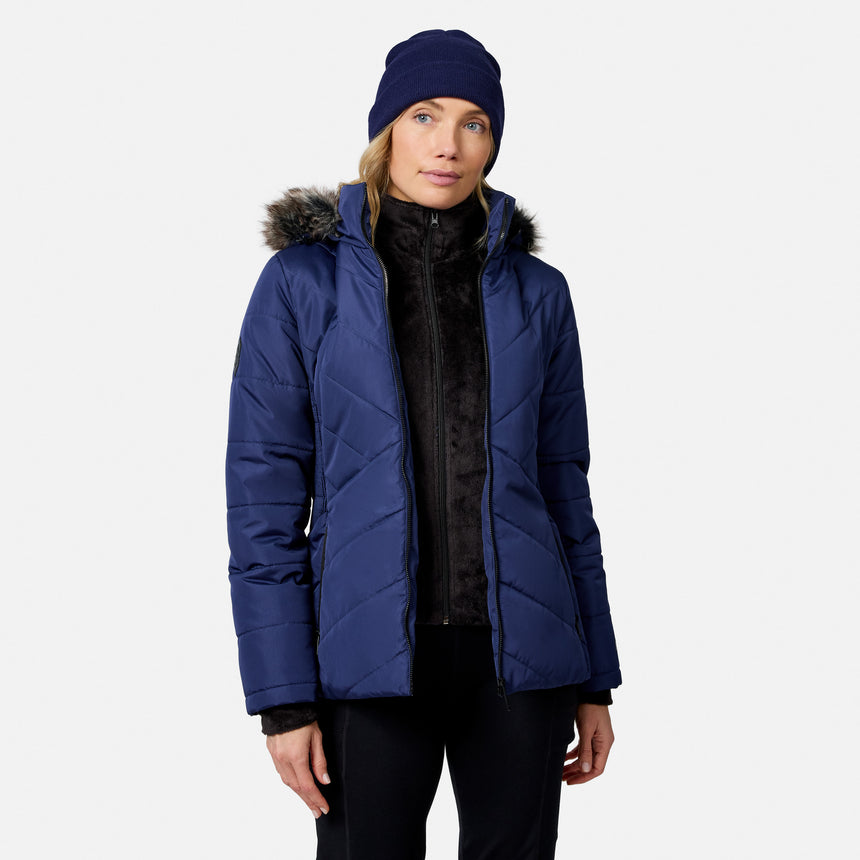 A woman wears a blue Free Country Women’s Brisk II Parka Jacket with a faux-fur trim hood and a matching blue beanie.