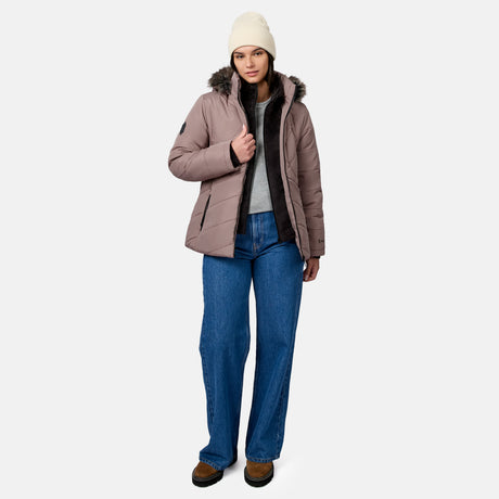 A person wearing a mauve Free Country Women’s Brisk II Parka Jacket with a faux-fur hood, a beige beanie, blue jeans, and brown boots.