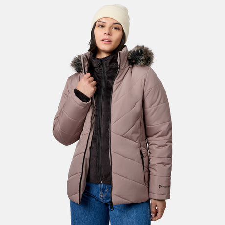 A woman wearing a mauve-colored Free Country Women’s Brisk II Parka Jacket with a faux-fur trimmed hood over a black zippered fleece jacket and a beanie.