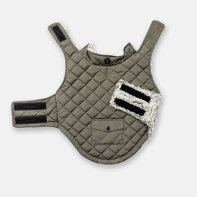 The Stratus Lite Reversible Dog Jacket by Clearance is an olive-green, quilted, wind-resistant jacket for dogs with black Velcro straps, a snap-button pocket, and white fleece lining, shown laid flat on a white background.