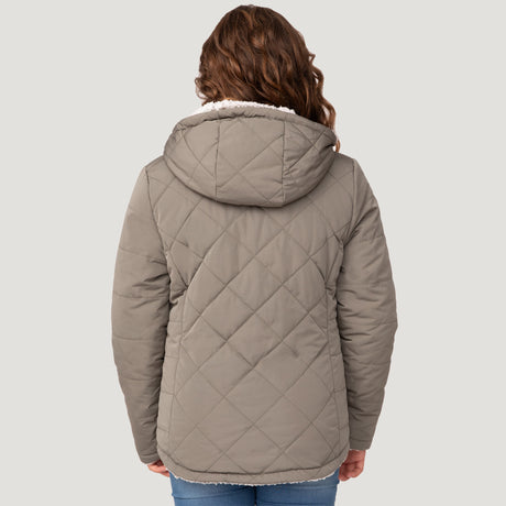 [Model is wearing a size Medium.] Girl wearing the Free Country Girls' Stratus Lite Reversible Jacket in grey, featuring a diamond quilted pattern and a sherpa lining with a plain yolk, standing and smiling with hands in pockets against a plain backdrop.