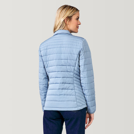 A blonde woman, seen from the back, wears the Clearance Women's FreeCycle® Lansby Packable Puffer Jacket in light blue with dark blue pants, standing against a plain light gray background.