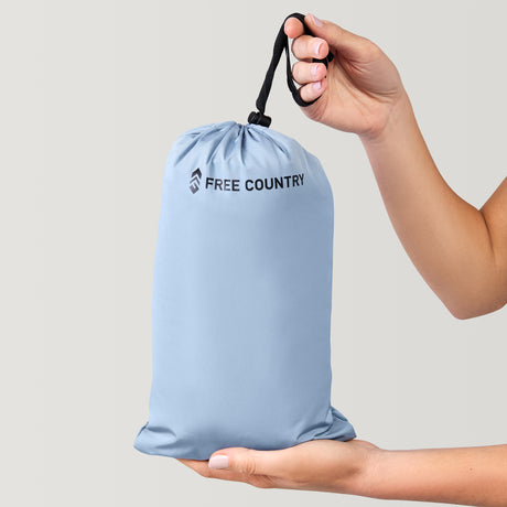 A person holds a light blue drawstring bag with "Clearance" and "Women's FreeCycle® Lansby Packable Puffer Jacket" on it, one hand on the handle and the other supporting the bottom, set against a neutral background.