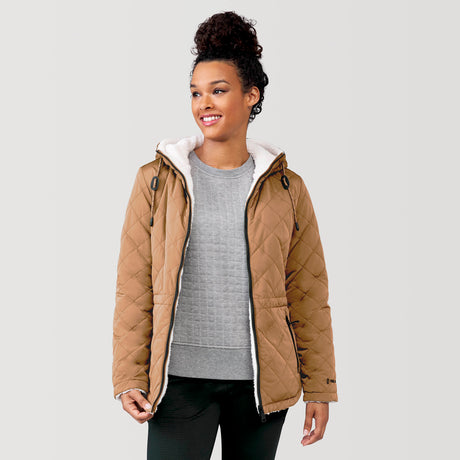 [Alexis is 5’6” wearing a size Small.] Woman wearing Free Country Women's Switch It Up Cloud Lite Reversible Jacket in tan with a full front zipper opening, attached hood with adjustable drawcord, diamond quilting, soft lining, and water resistant and wind resistant stretch performance fabric. light grey background. Perfect women’s  jacket for fall weather.