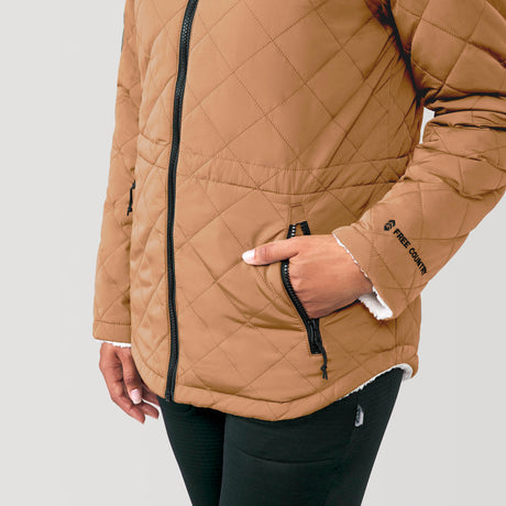 [Alexis is 5’6” wearing a size Small.] Woman wearing Free Country Women's Switch It Up Cloud Lite Reversible Jacket in tan with a full front zipper opening, attached hood with adjustable drawcord, diamond quilting, soft lining, and water resistant and wind resistant stretch performance fabric. light grey background. Perfect women’s  jacket for fall weather.