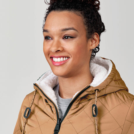 [Alexis is 5’6” wearing a size Small.] Woman wearing Free Country Women's Switch It Up Cloud Lite Reversible Jacket in tan with a full front zipper opening, attached hood with adjustable drawcord, diamond quilting, soft lining, and water resistant and wind resistant stretch performance fabric. light grey background. Perfect women’s  jacket for fall weather.