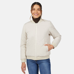 A woman smiles with one hand in her pocket, wearing the Clearance Women's Stratus Lite Reversible Quilted Bomber Jacket over a brown turtleneck and blue jeans against a plain white background.
