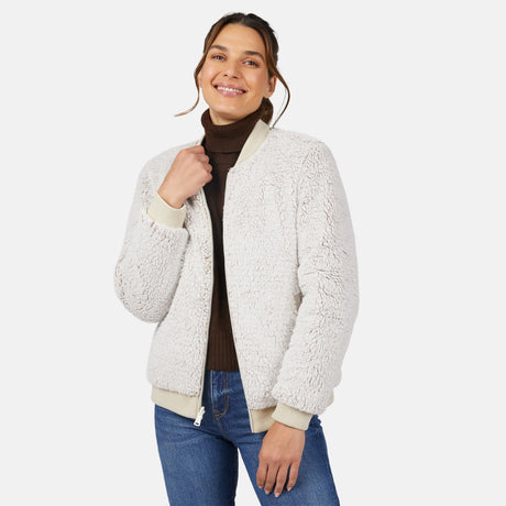 A woman smiles while wearing the Clearance Women's Stratus Lite Reversible Quilted Bomber Jacket over a dark brown turtleneck and blue jeans, standing against a plain white background.