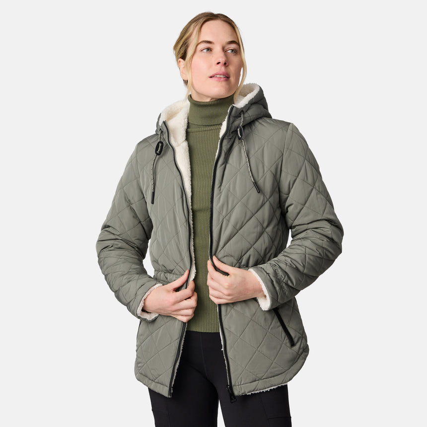 [CJ is 5'10" wearing size S.] Woman wearing Free Country Women's Switch It Up Cloud Lite Reversible Jacket in green with a full front zipper opening, attached hood with adjustable drawcord, diamond quilting, soft lining, and water resistant and wind resistant stretch performance fabric. light grey background. Perfect women’s  jacket for fall weather.
