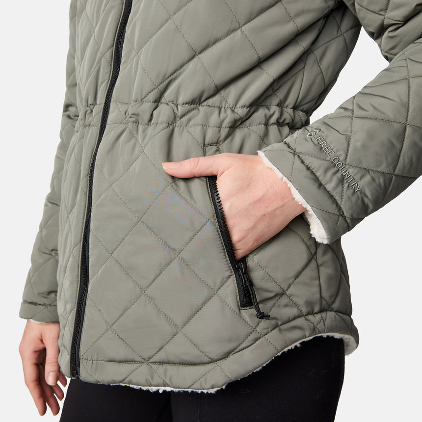 [CJ is 5'10" wearing size S.] Woman wearing Free Country Women's Switch It Up Cloud Lite Reversible Jacket in green with a full front zipper opening, attached hood with adjustable drawcord, diamond quilting, soft lining, and water resistant and wind resistant stretch performance fabric. light grey background. Perfect women’s  jacket for fall weather.