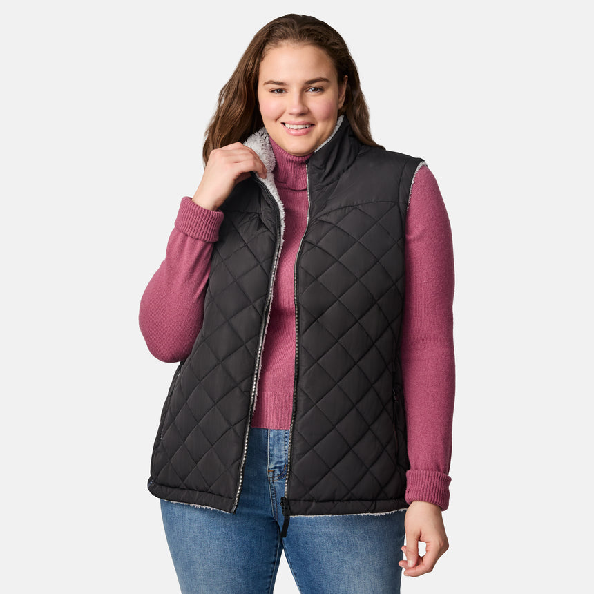 [Karissa is 5'9.5" wearing size 1X.]  Women’s Free Country black diamond-quilted vest with zip-front closure—reverses to cozy sherpa for added warmth and texture. Worn open over a pink knit sweater and blue jeans for a relaxed, cold-weather look.