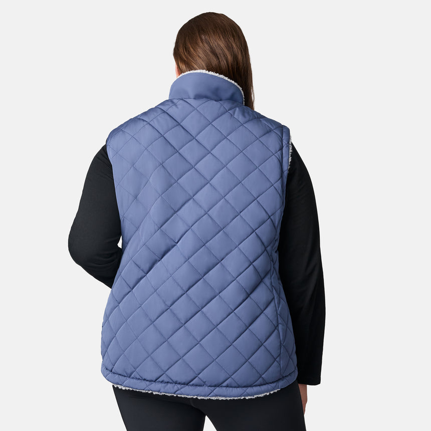[Karissa is 5'9.5" wearing size 1X.] Women’s Free Country blue quilted vest with zip-front closure and zippered pockets—reverses to cozy sherpa for added warmth and texture. Worn over a black long-sleeve shirt and blue pants for a casual, transitional-weather look.